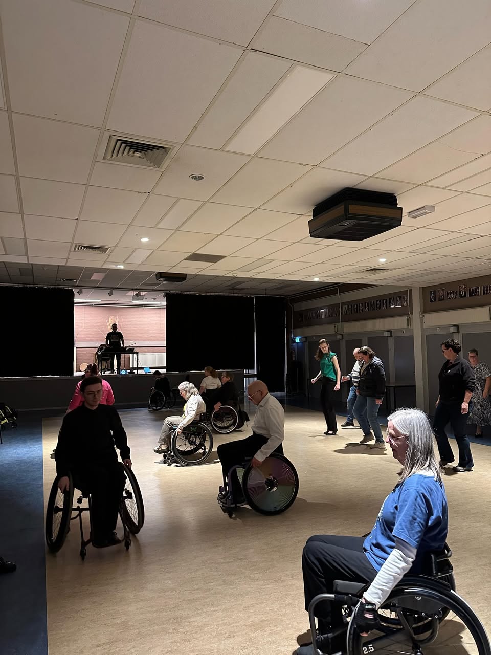 Deelnemers met en zonder rolstoel dansen samen in een zaal